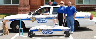 Jay Warnick, an eleven year-old from Drayden, poses in his soap box derby car which is modeled after a St. Mary's County Sheriff's Office K-9 unit. Pictured with his father Jim and his mother Colette. Sheriff Cameron is seated in the patrol car.