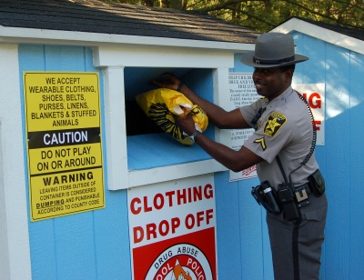 DFC Phil Foote, the full time DARE Officer for the Calvert County Sheriff's Office, places a bag of clothing into a recycling bin at the Ball Road refuse site. The program receives an annual contribution from the recycler for each container. (Submitted photo)
