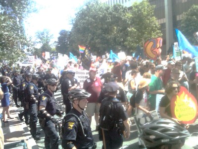 Police in bike helmets line street with parade of demonstrators.