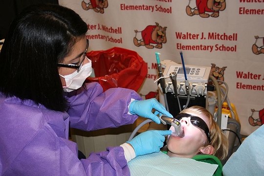 Celeste Camerino, the oral health program coordinator with the Charles County Department of Health assists Dr. Helen Lee-Virgil place dental sealants on Brett Wilkinson, a second grade student at Walter J. Mitchell Elementary School. Dental sealants can prevent 70 percent of tooth decay, according to the Surgeon General. (Photo: CCPS)