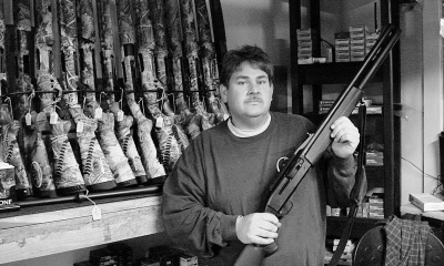 Damian Hall, owner of D’s Outdoor and Pawn on Point Lookout Road, holds a military-style shotgun that represents the kind of firearms he’s been selling lately in large numbers after the presidential election. The hunting shotguns in the background have been selling slowly. (Photo: Guy Leonard)