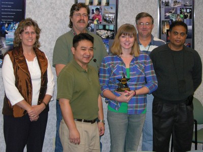 Human Systems Integration engineers left to right - Robyn Ryan, Alex Salunga, Isabel Anderson, Ajoy Muralidhar stand in front of Robert Hamburger and Jon Dachos - at NSWC Dahlgren after they were honored for superior support to the CVN 78 (Gerald R. Ford next generation carrier) Program as key players in the Warfare System Engineering Technical Team. Anderson holds the NAVSEA Excellence Award presented to the team by Vice Adm. Kevin McCoy, commander, Naval Sea Systems Command, in Washington D.C. Dec. 7. 