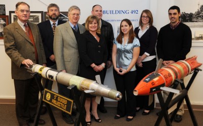 The Dahlgren History Team gathers around two projectiles at the Naval Surface Warfare Center Dahlgren Division (NSWCDD), left to right: Wayne Harman, Brad Johnson, Robin Staton, Stacia Courtney, Jim Poynor, Karen Lauterbach, Amelia Toms and Greggory DiSalvo.