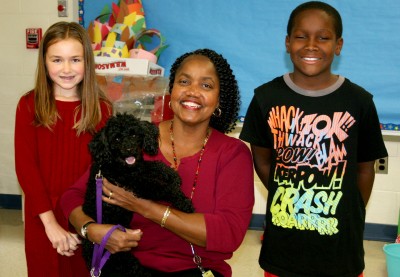 T.C. Martin Elementary School fourth graders Linsey Anderson, left, and Quinnel Booth, right, meet Corbin, a four-year-old poodle from the Charles County Humane Society who benefited from funds raised to help animals in need of advanced medical treatment. Students held a penny drive to collect donations, which was coordinated by Melody Philpotts, library media specialist, pictured holding Corbin. Anderson and Booth helped collect donations daily at school. (Submitted photo)