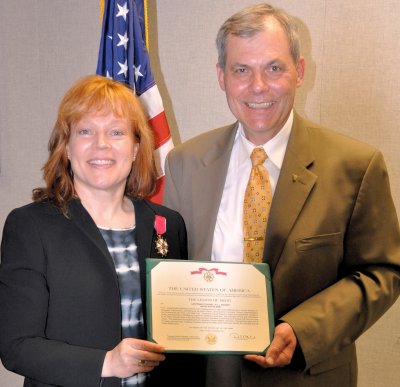 Lt. Col. Jill Wagner, U.S. Army Ret., displays her Legion of Merit award citation with Martin Westphal - Vice Director for Director Command, Control, Communications and Computers/Cyber, Joint Staff - at the Naval Surface Warfare Center Dahlgren Division (NSWCDD) weekly leadership team meeting April 14. The award honored Wagner for exceptionally meritorious service over a distinguished career serving in various positions of increasing responsibility, culminating as the Action Officer, Directorate for Command, Control, Communications and Computers / Cyber (C4), Joint Staff (J-6). In her new role as a NSWCDD Asymmetric Defense Systems Department senior systems analyst, Wagner identifies operational requirements for the Mission Assurance Decision Support System, which supports U.S. Navy and joint warfighting communications missions across the world. U.S. Navy photo by John Joyce (Released)