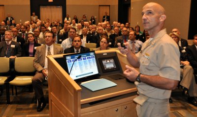 Capt. Brian Durant presents a command brief to attendees. (U.S. Navy photo by John Joyce/Released)