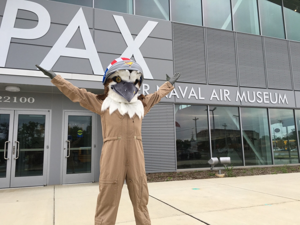 Oscar Falco, the new mascot for the Patuxent River Naval Air Museum, "spreads his wings" in front of the iconic hangar-style museum building that was opened this past spring. Pax Museum photo by Amy Davis.
