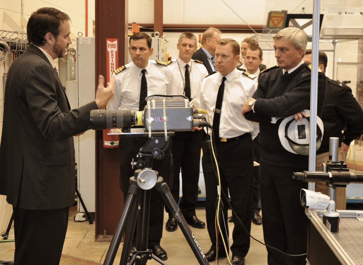 British Royal Navy First Sea Lord Adm. Sir Philip Jones is briefed on U.S. Navy high energy laser programs by Dr. Chris Lloyd, High Energy Laser Lethality lead at Naval Surface Warfare Center Dahlgren Division (NSWCDD). Lloyd explained the importance of rigorous modeling and laboratory testing against target materials to ensure high energy laser systems are built that meet the requirements of the warfighter once fielded. More than 18 NSWCDD subject matter experts briefed Jones and his delegation on programs that included HSI, gun systems, ballistic missile fire control, directed energy, and electric weapons such as the Laser Weapon System. (Photo: John Joyce)