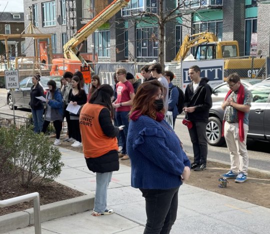 WASHINGTON --- A Catholic University group prays with other protesters outside NoMa Planned Parenthood on Feb. 12. A patient escort, wearing an orange vest and who asked not to be identified for safety concerns, waits for patients at the front stairs of the clinic beside anti-abortion activist Lauren Handy (in foreground, right). (Photo: Emily Hahn)